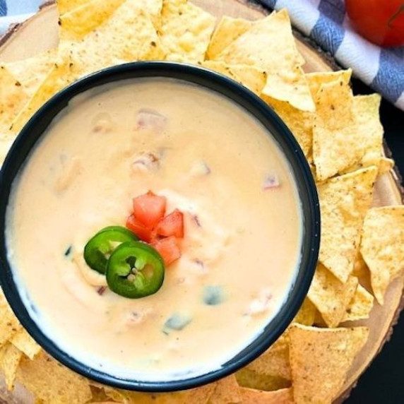 Nacho dip in a black bowl with tortilla chips spread around the bowl. 