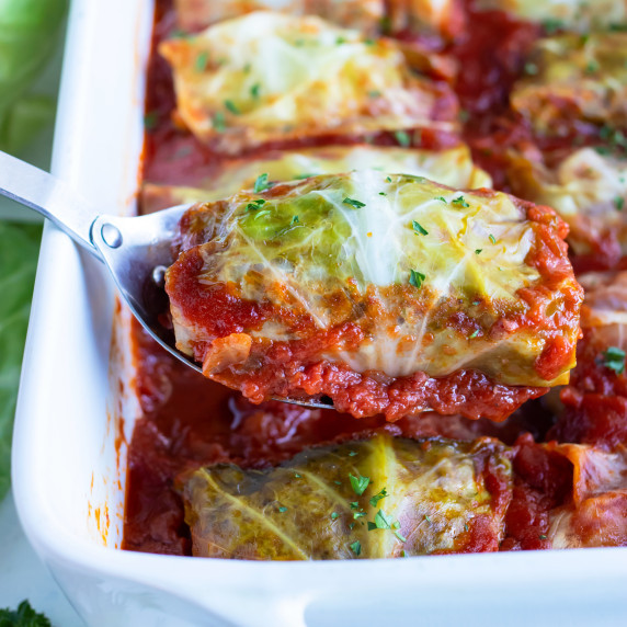 Stuffed Cabbage Rolls RECIPE in a white dish scooped out with a metal spoon.