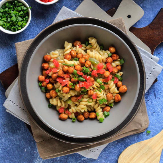 Bowl of pasta topped with chickpeas, tomatoes and green onions