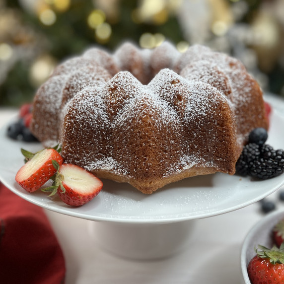 Bundt cake on a white cake plate garnished with powdered sugar and fresh berries.