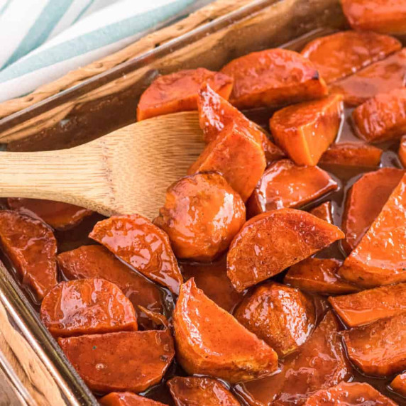 Close up candied yams in a pan with a wooden spoon scooping.