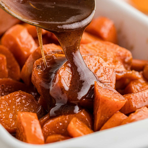Close up of some candied yams with a treacle like sauce being poured over the top.