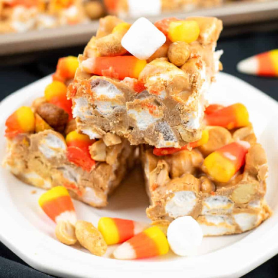 Three bars stacked on a plate with more candy corn, marshmallows and peanuts nearby on the plate.