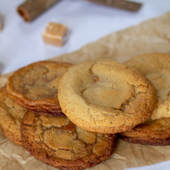 Caramel Stuffed- Apple Cider Cookies on parchment with cinnamon sticks