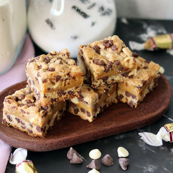 Several caramel chip bars arranged on a small wooden platter with a few ingredients scattered around