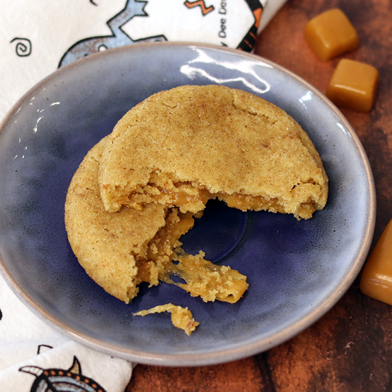 Caramel stuffed snickerdoodle broken open on a blue plate to show caramel interior.