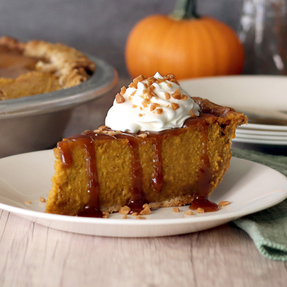 A slice of caramel toffee pumpkin pie topped with caramel, whipped cream and a sprinkle of toffee