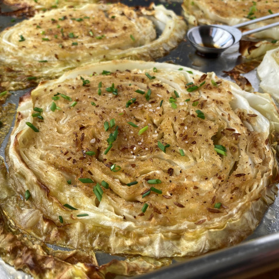 Slice of roasted cabbage topped with chives on a sheet pan.