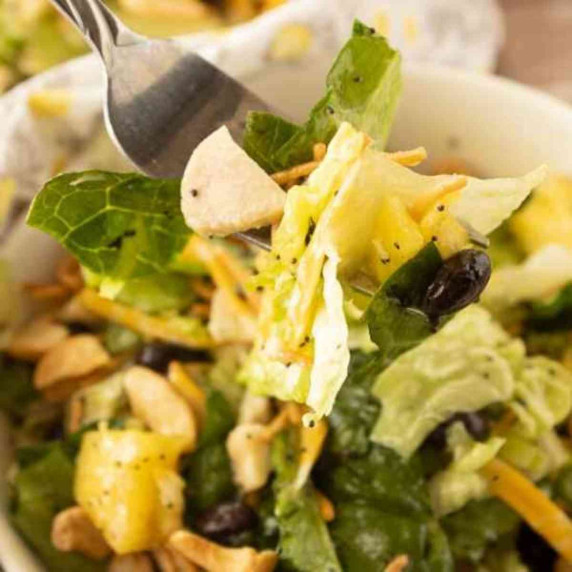 A forkful of lettuce, chicken, pineapple, black beans and cashews coated in poppy seed dressing.