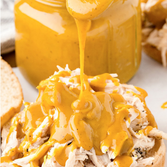 Mustard-based bbq sauce being drizzled on top of pulled chicken.