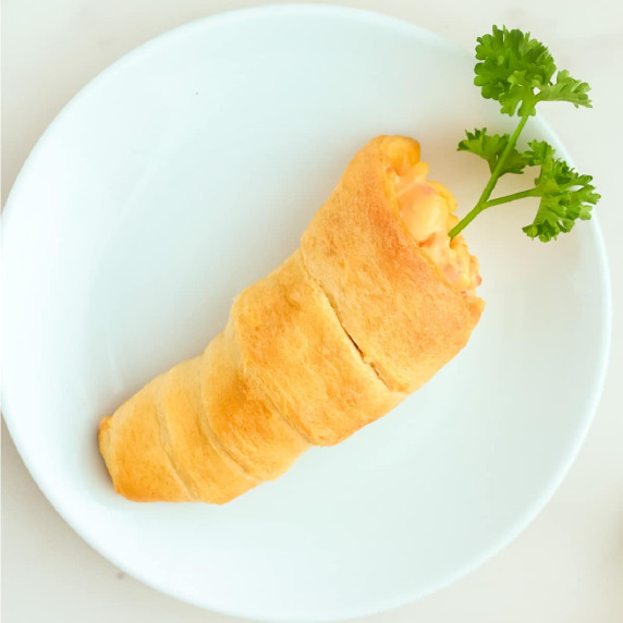 A carrot shaped crescent roll with a parsley as a carrot top on a plate.
