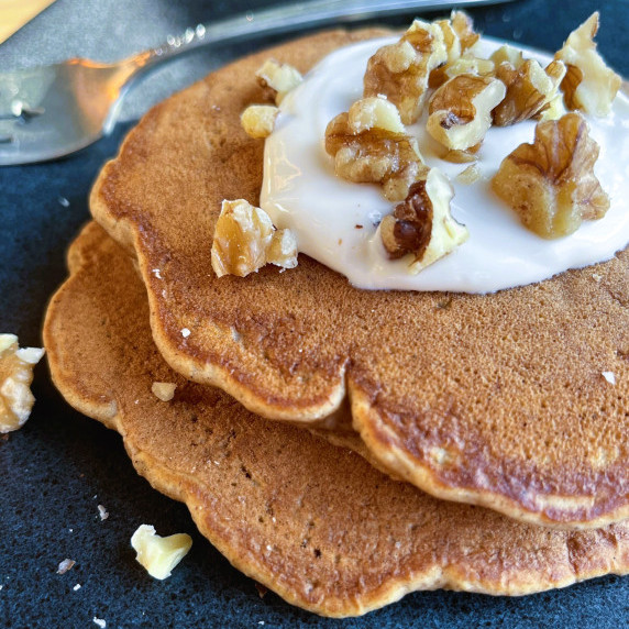Pancakes topped with cream cheese topping and walnuts on a gray plate.