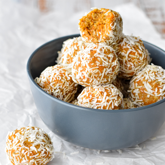 a navy bowl of carrot cake protein balls with a bite taken out of the top ball