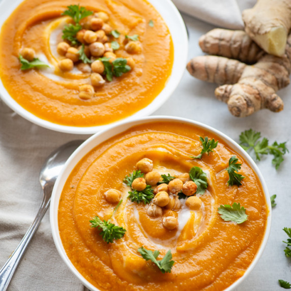 Two bowls of carrot-ginger soup garnished with toasted chickpeas and cilantro.