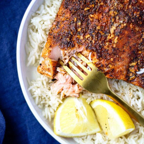 A salmon fillet on rice with lemon wedges.