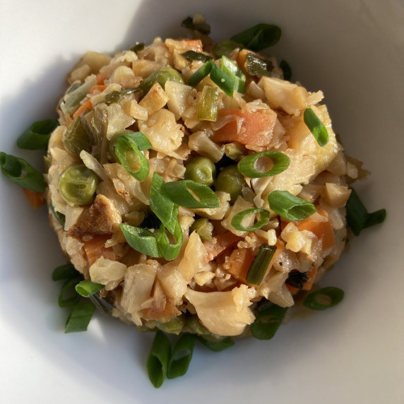 Cauliflower fried rice topped with sliced scallions in a white bowl. 