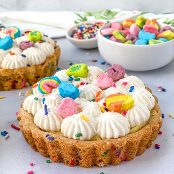 Cereal Milk Tartlet with Lucky Charms marshmallows and sprinkles on top and scattered nearby.