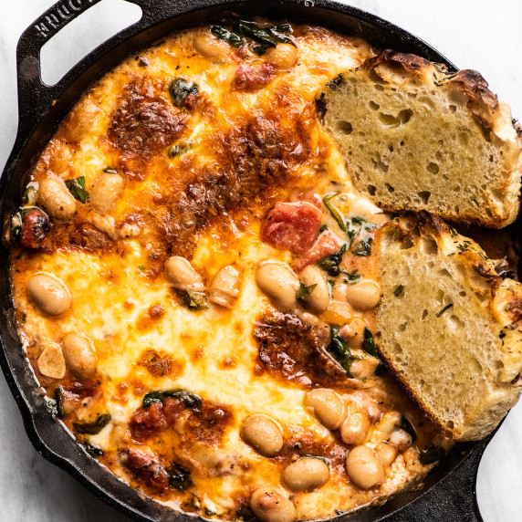 white beans in a tomato sauce with cheese and sliced of bread in a cast iron pan
