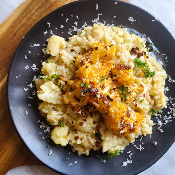 Cheesy risotto with roasted cauliflower on a black plate against a wooden background.