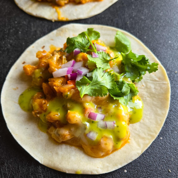 White corn tortilla filled with cheesy hominy, red onions, green salsa and green cilantro.