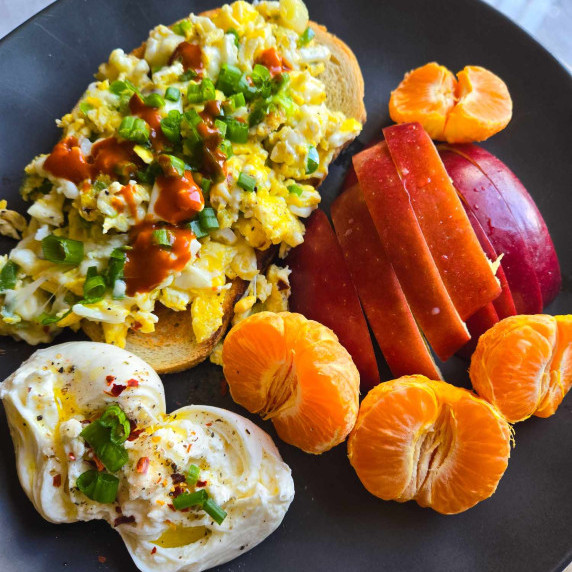 An assortment of colourful eats including fruit, burrata, and egg scram toast on a black plate