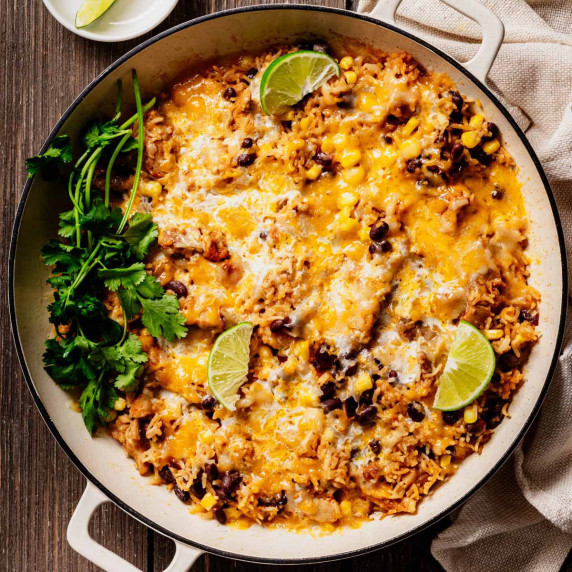 A skillet filled with cheesy Mexican chicken and rice, topped with melted cheese, black beans, corn,