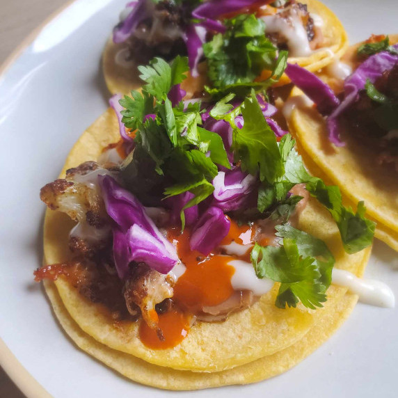 Yellow corn tortillas topped with red hot sauce, purple cabbage, and greens