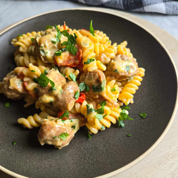 A creamy plate of sausage fusilli with green parsley on a matte black plate.