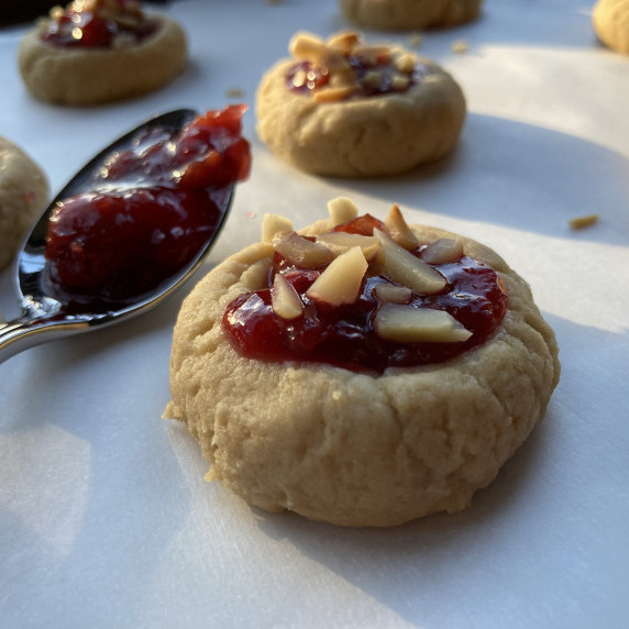 Thumbprint cookies filled with cherry jam and topped slivered almonds on a white platter.