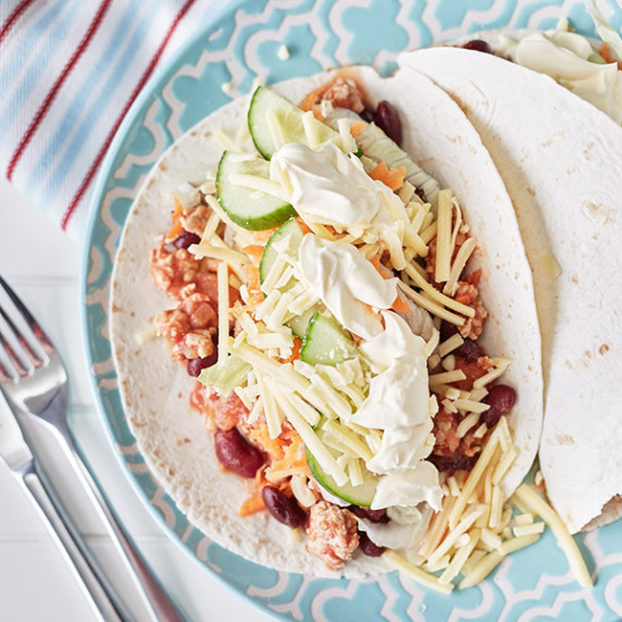2 Tortilla wraps topped with cooked chicken mince, beans, grated cheese, salad and sour cream.