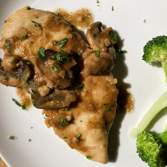 Chicken marsala on a white plate with steamed broccoli.