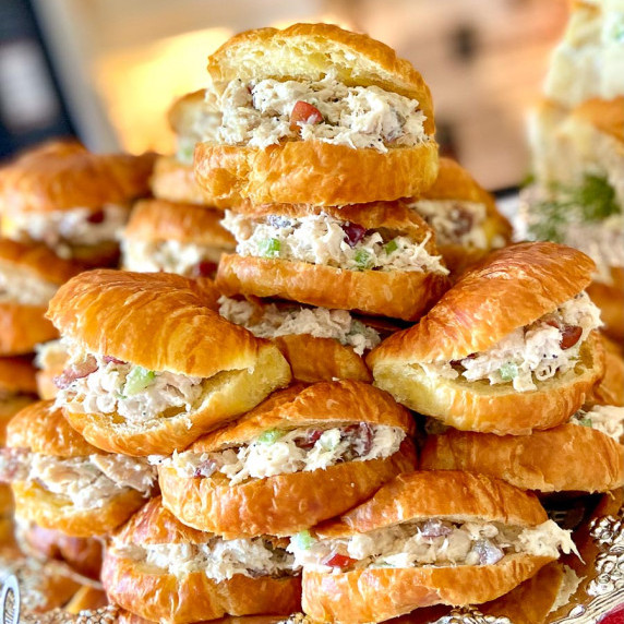 Chicken salad sandwiches on croissants stacked on serving platter.
