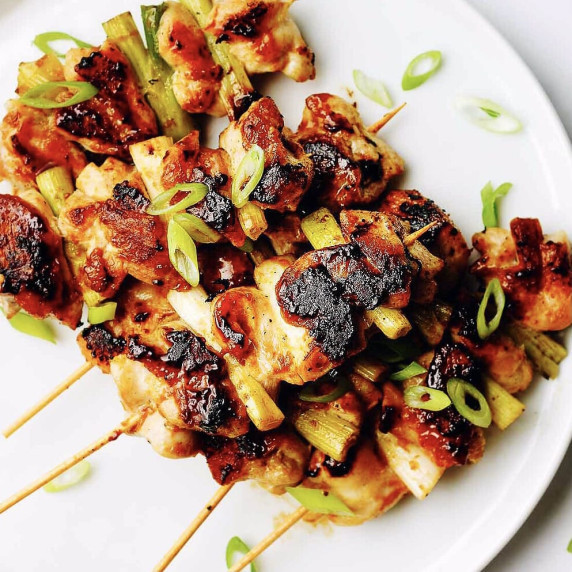 Grilled chicken skewers garnished with scallions on a white plate 