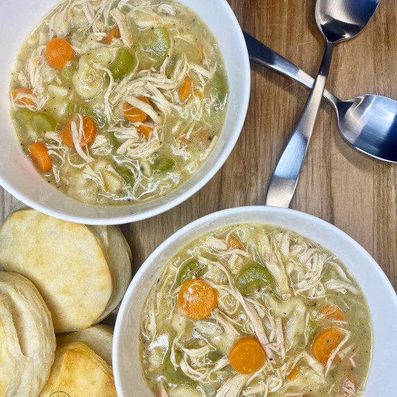 Bowl of soup with pulled chicken, carrots, celery, onions, dumplings and biscuits on the side