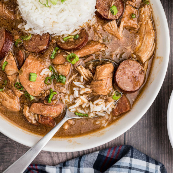 a bowl with chicken and sausage gumbo with a spoon and a little rice
