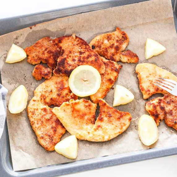 Breaded chicken schnitzels on a baking tray decorated with slices of lemon 