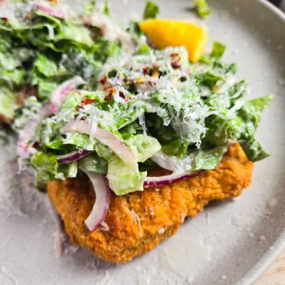 Golden, plant-based chik'n patty topped with green salad with red onions.