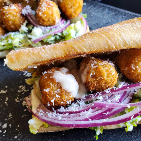 Golden brown baguette stuffed with purple onions, white dressing, green romaine, golden chik'n bites