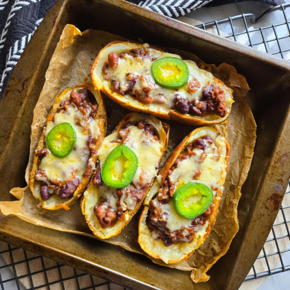 A parchment lined tray with 4 chili cheese stuffed potato skins against a black towel.