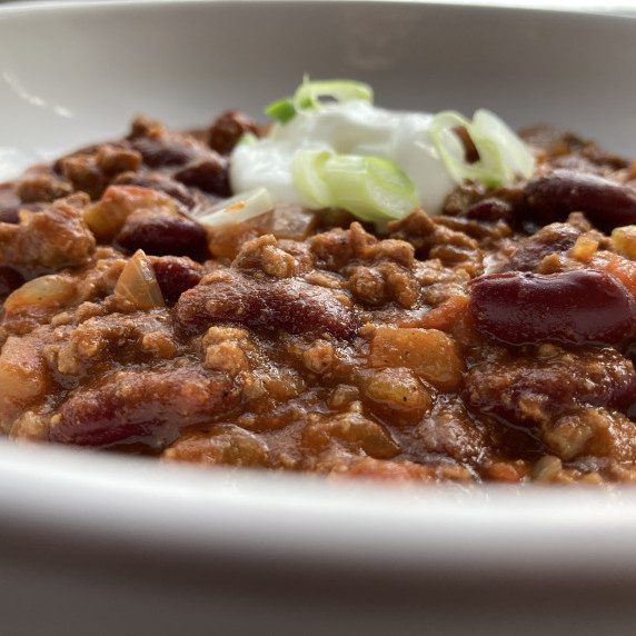 Bowl of beef and bean chili topped with sour cream and sliced green onions.