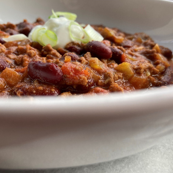 Beef stew garnished with fresh minced parsley in a white bowl.