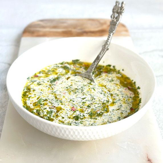 A white bowl filled with chimichurri mayo, showing specks of green fresh herbs and red chili 