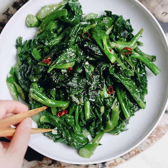 Chinese broccoli and red chili pepper in a white bowl with chopsticks