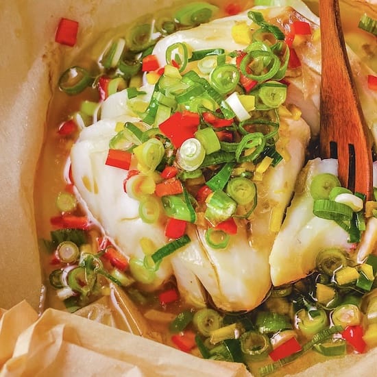 Cod fish, green onions and red peppers in parchment paper with wooden serving fork