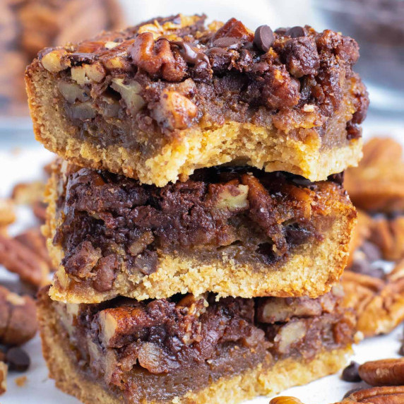Chocolate Pecan Pie Bars RECIPE stacked up on each other with pecans in the background.