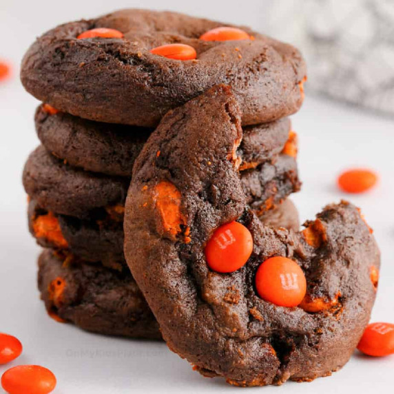 Stack of chocolate cookies with orange candies, one cookie has a bite missing.