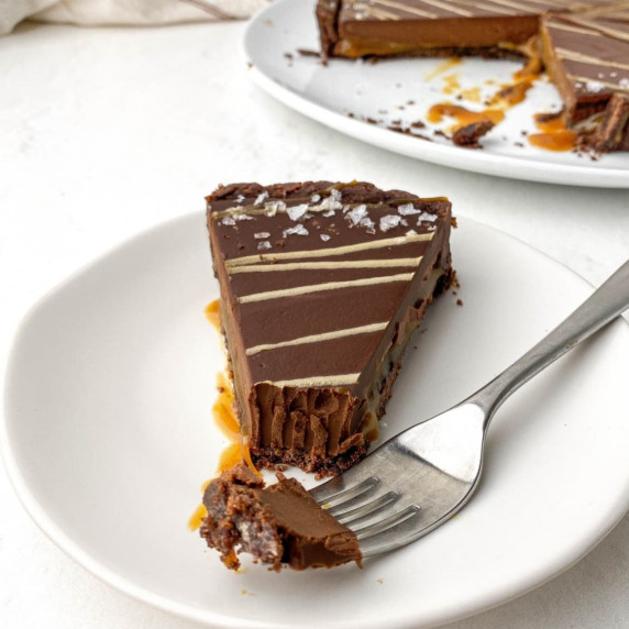 slice of chocolate caramel tart on a white plate with a fork next to it