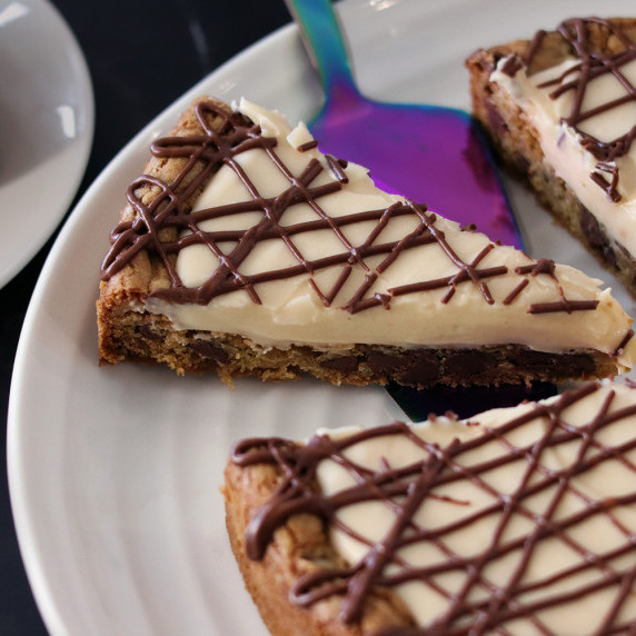 A slice of Chocolate Chip Cookie Tart on a white plate on a black marble counter.