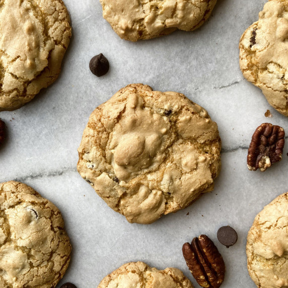 Chocolate chip cookies on a marble board with pecans and chocolate chips.