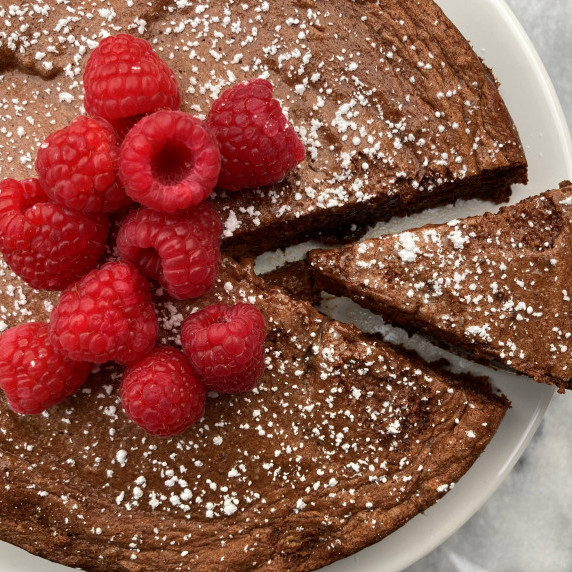 Chocolate mousse cake topped with raspberries on a white cake plate on a marble countertop.